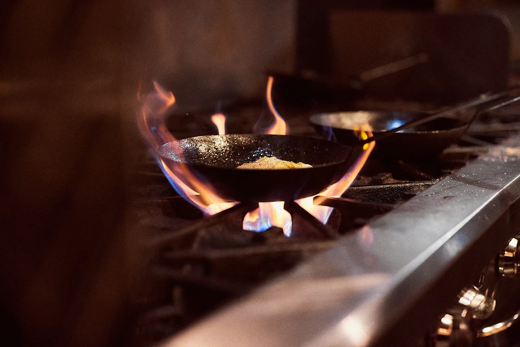Frying pan with food cooking on a gas stovetop with bright flames.