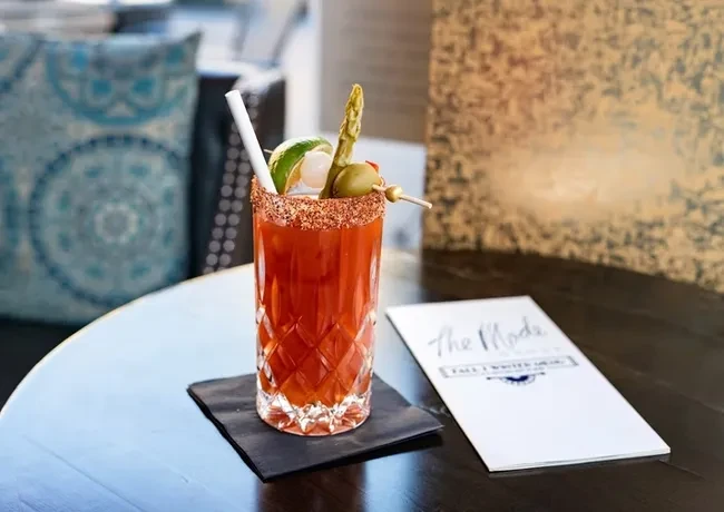 Red cocktail with spiced rim, diverse garnishes, and 'The Mode' menu.