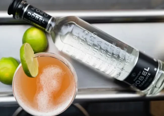 Orange cocktail, Maestro Dobel tequila bottle, and limes.
