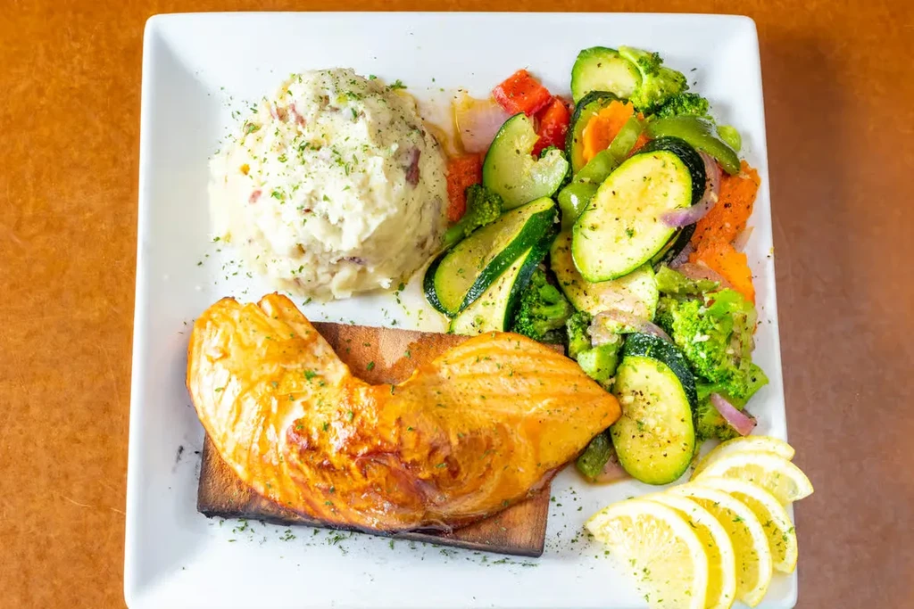 Well-plated salmon, mashed potatoes, sautéed vegetables, and lemon on a white dish.