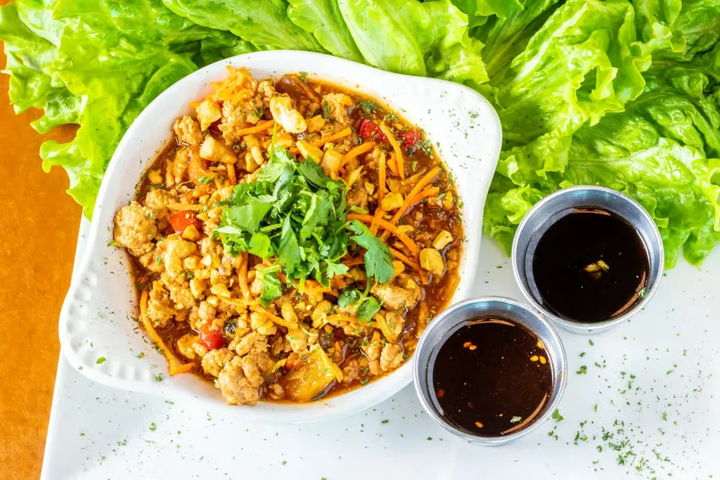 Lettuce wraps dish with meat filling, fresh leaves, and dipping sauces.