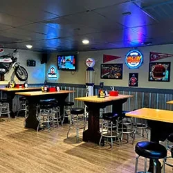 Empty, dimly lit bar with high-top tables, motorcycle, and neon signs.