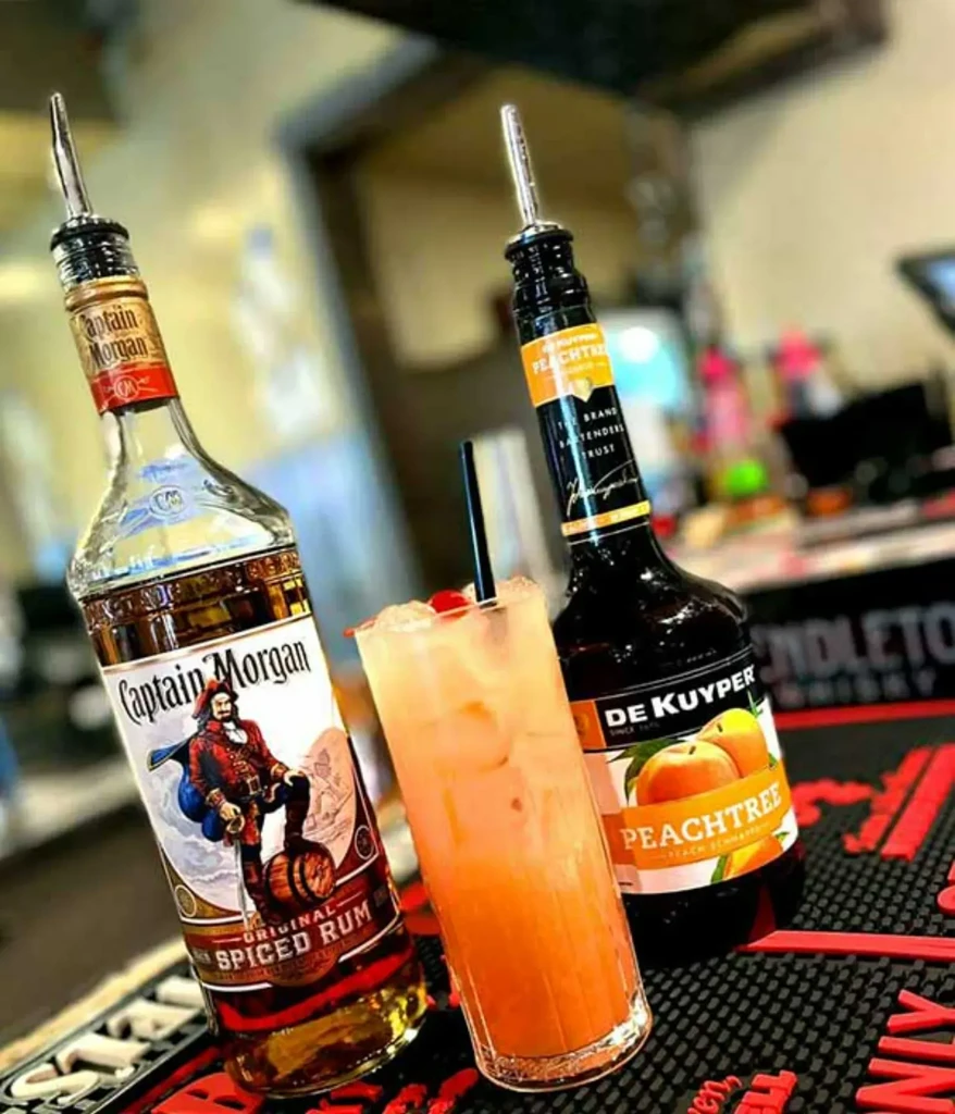 Captain Morgan and Peachtree Peach Schnapps bottles, garnished cocktail on mat.