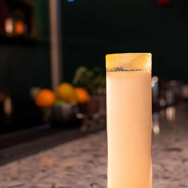 Tall glass with bubbly opaque beverage and golden sugar rim.