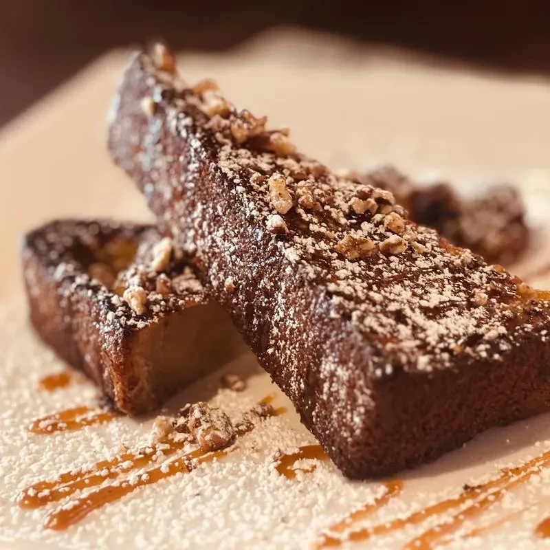 Two thick French toast sticks with powdered sugar, nuts, and caramel.