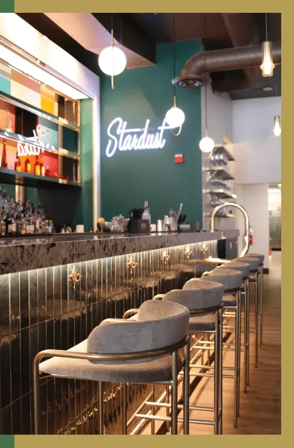 "Stardust" neon sign above a dark bar with empty stools.