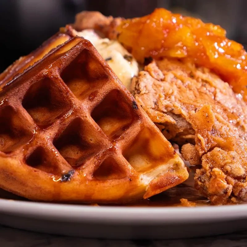 Crispy golden-brown chicken and waffles with syrup, sauce, and fruit.