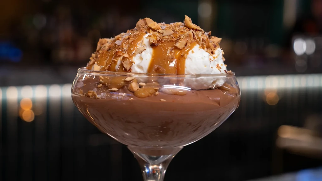 Dessert in glass: layered base, whipped cream, caramel, nuts, coconut.
