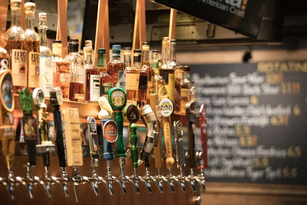 Close-up of shiny beer taps and liquor bottles at a well-stocked bar.