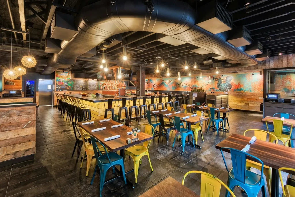 Industrial-chic restaurant interior with colorful murals, wooden tables, and a bar.