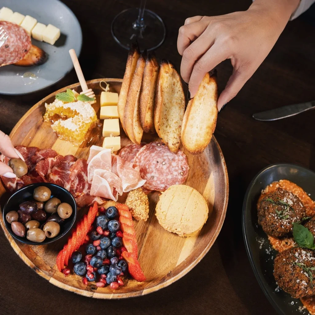 Hands picking food from a charcuterie board and other dishes.