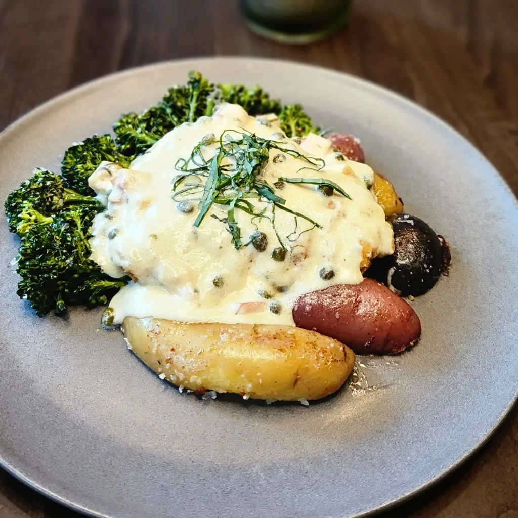 Plate of protein with creamy caper sauce, broccoli, and roasted potatoes.