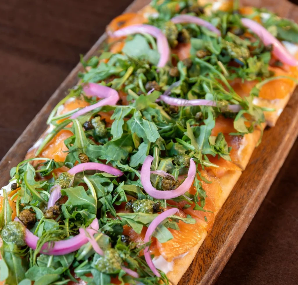 Flatbread with smoked salmon, arugula, red onion, capers on a wood board.
