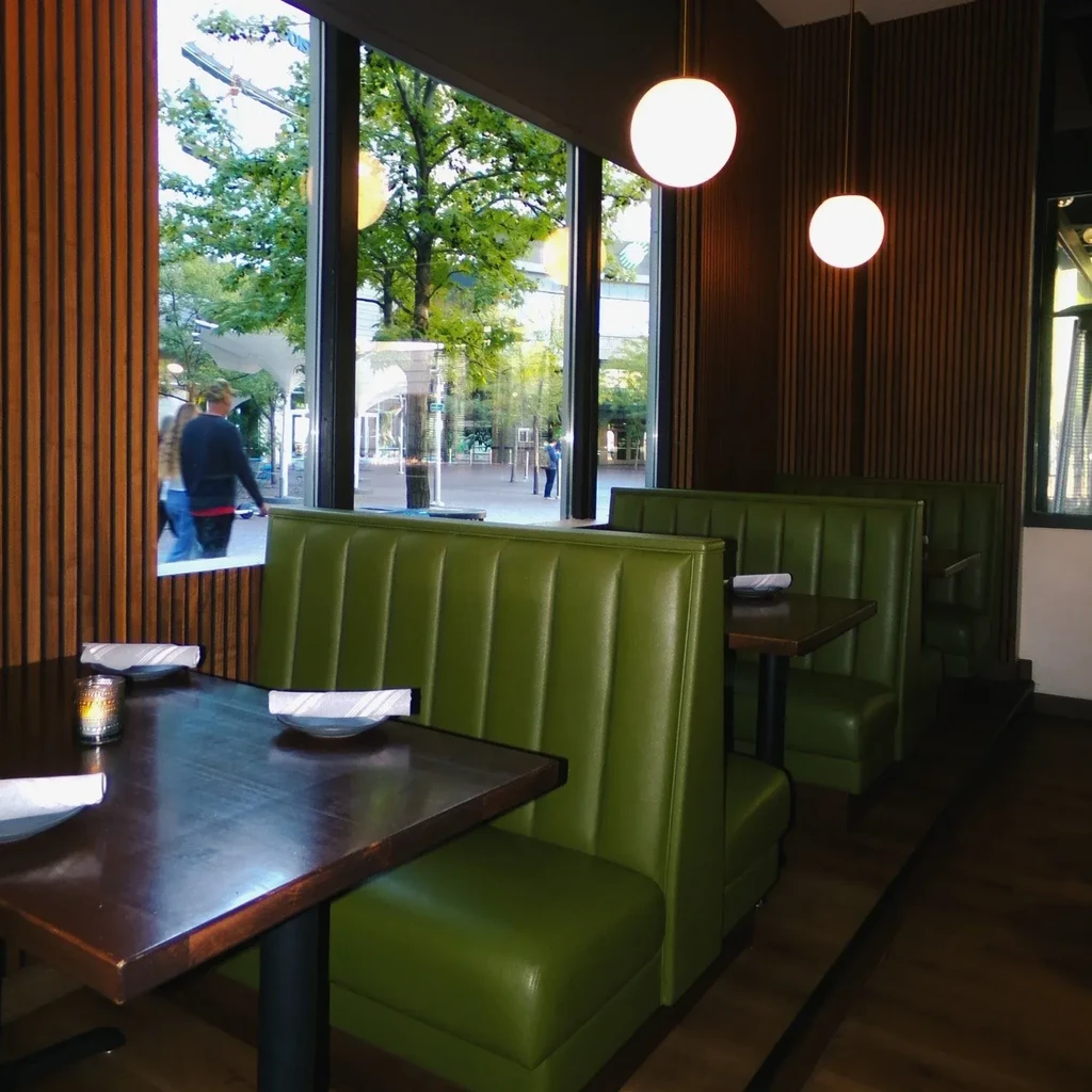 Modern restaurant interior: olive-green booth, wood panels, and city street view.