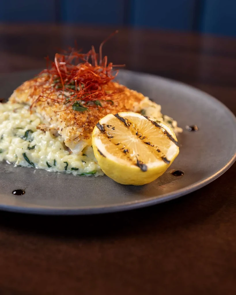 Pan-seared fish with chili threads, herb risotto, and charred lemon.
