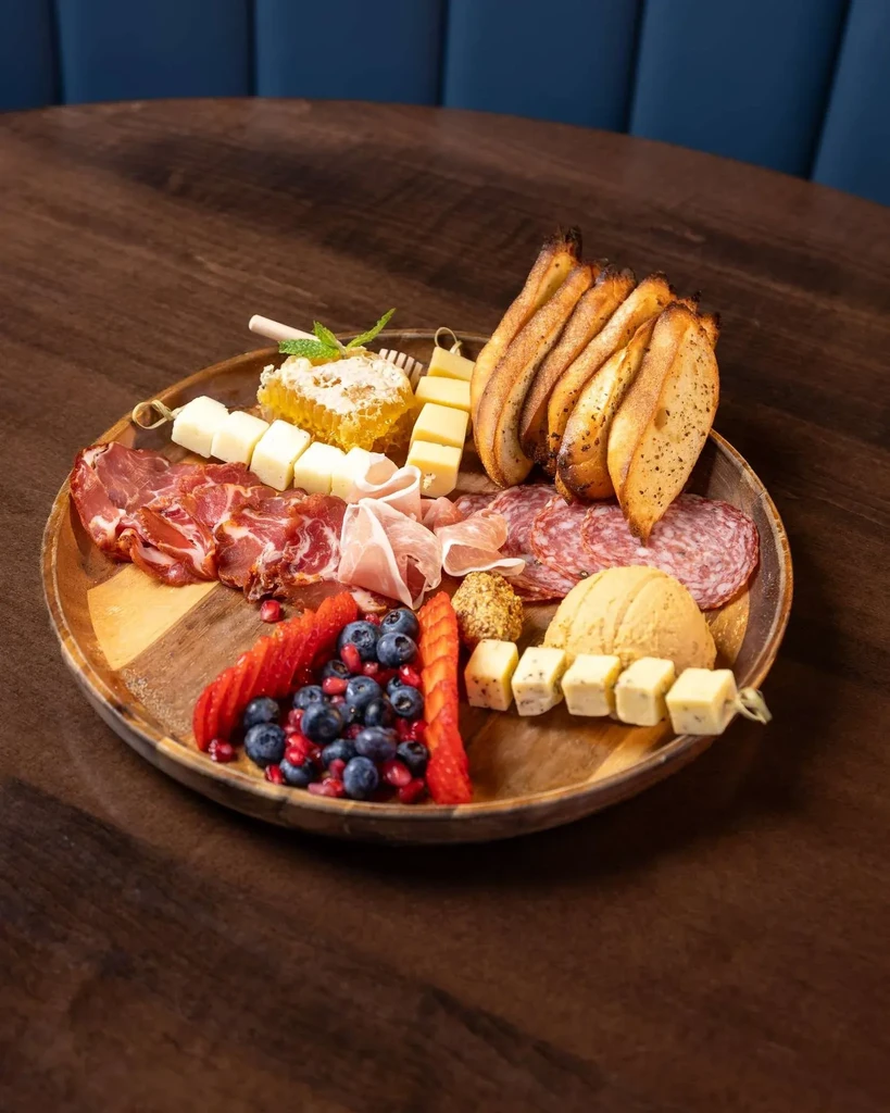 Overflowing charcuterie and cheese board with meats, cheeses, fruit, bread, honeycomb.