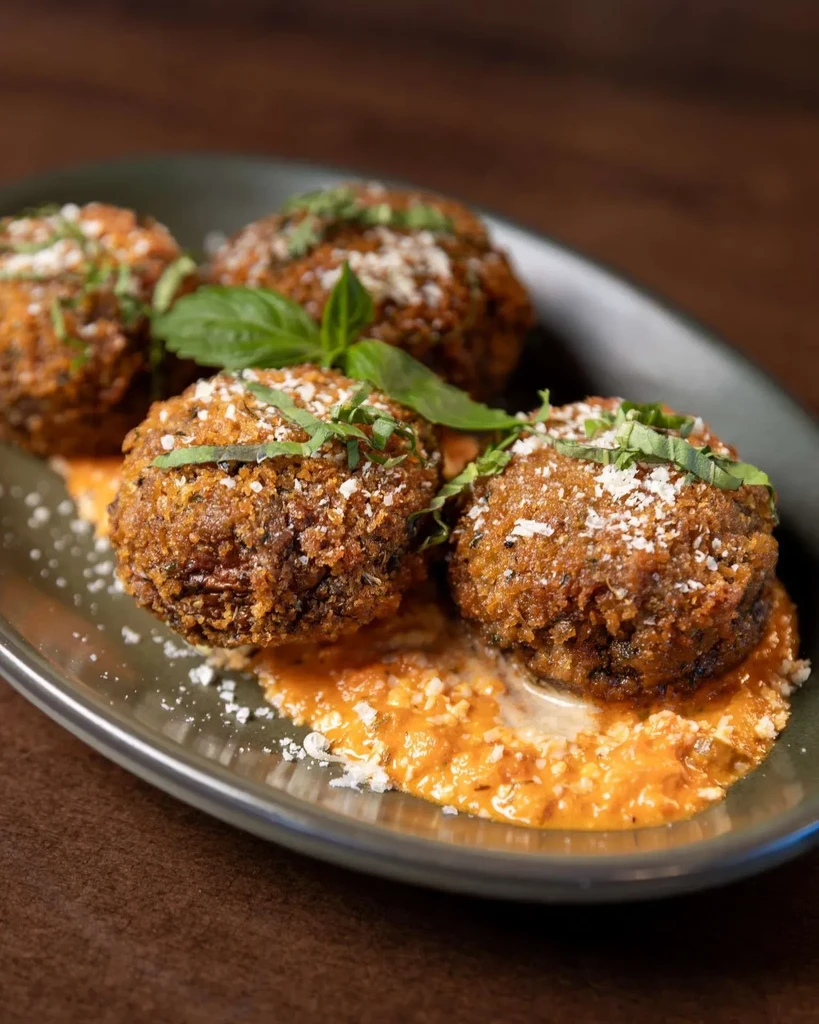 Four crispy deep-fried balls with cheese and herbs on orange sauce.