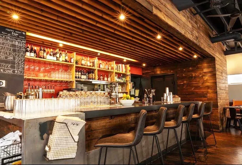 Well-lit, empty rustic-industrial bar with concrete counter and liquor display.