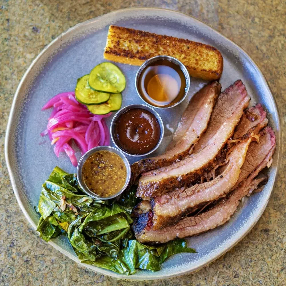 Well-presented plate of sliced brisket with sides and dipping sauces.