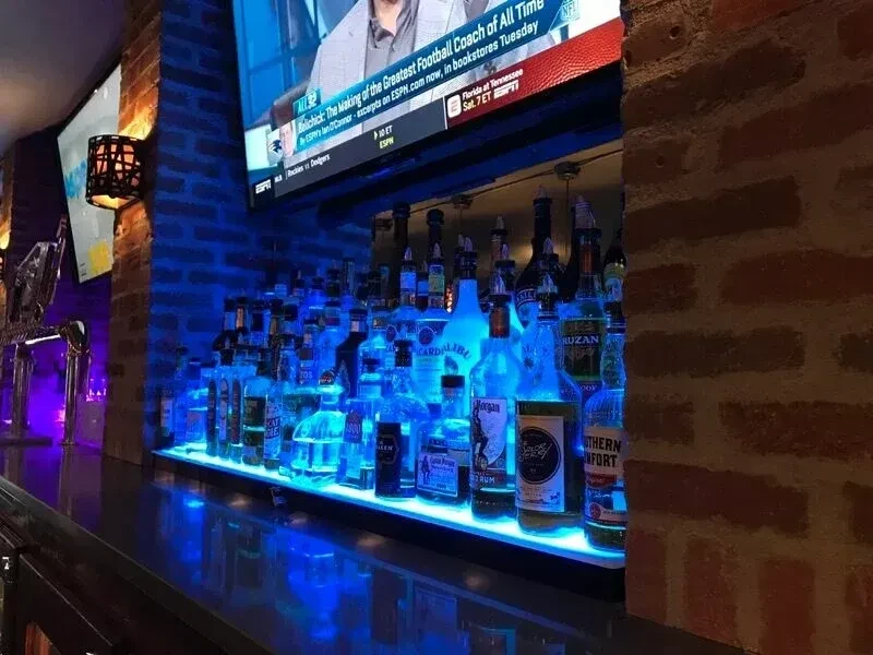 Modern bar with blue-lit liquor bottles, dark counter, and TV.