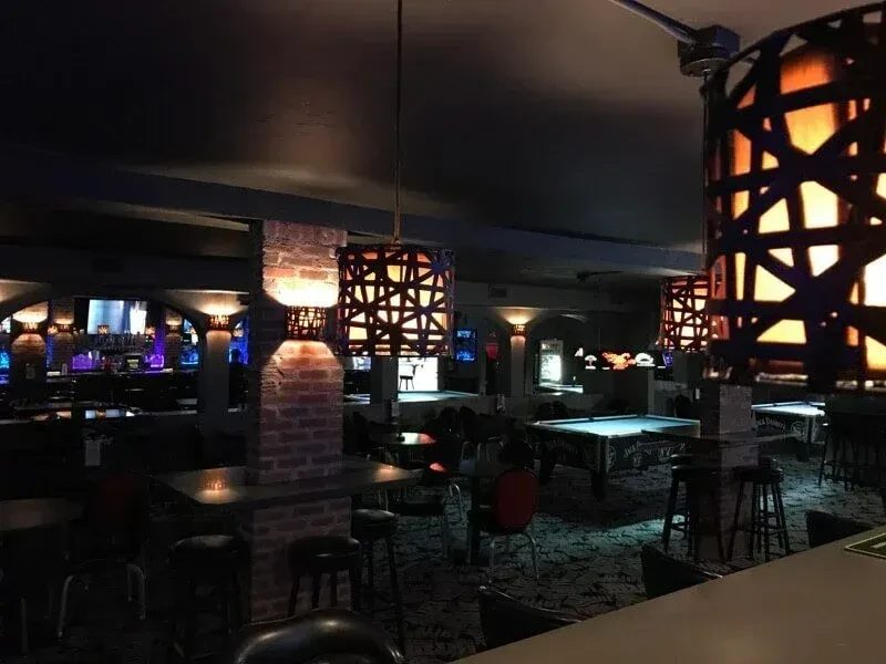 Moody bar with pool tables, a blue-lit bar, and orange lamps.