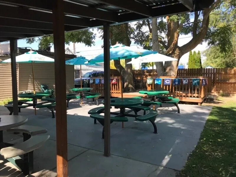 Concrete patio with green picnic tables, blue umbrellas, sports banners.