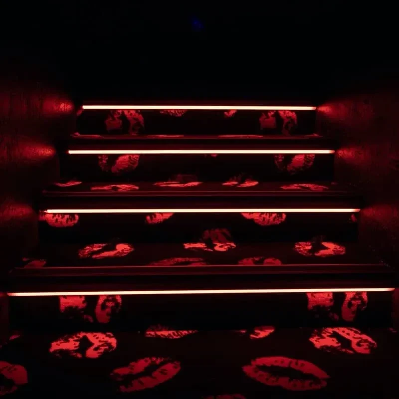 Dark staircase with red neon lights illuminating a kiss-print carpet.