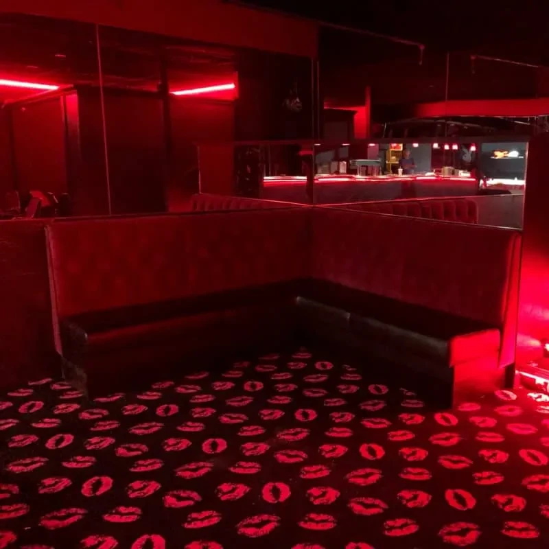 Red-lit bar interior with booth, lips carpet, and mirrored walls.