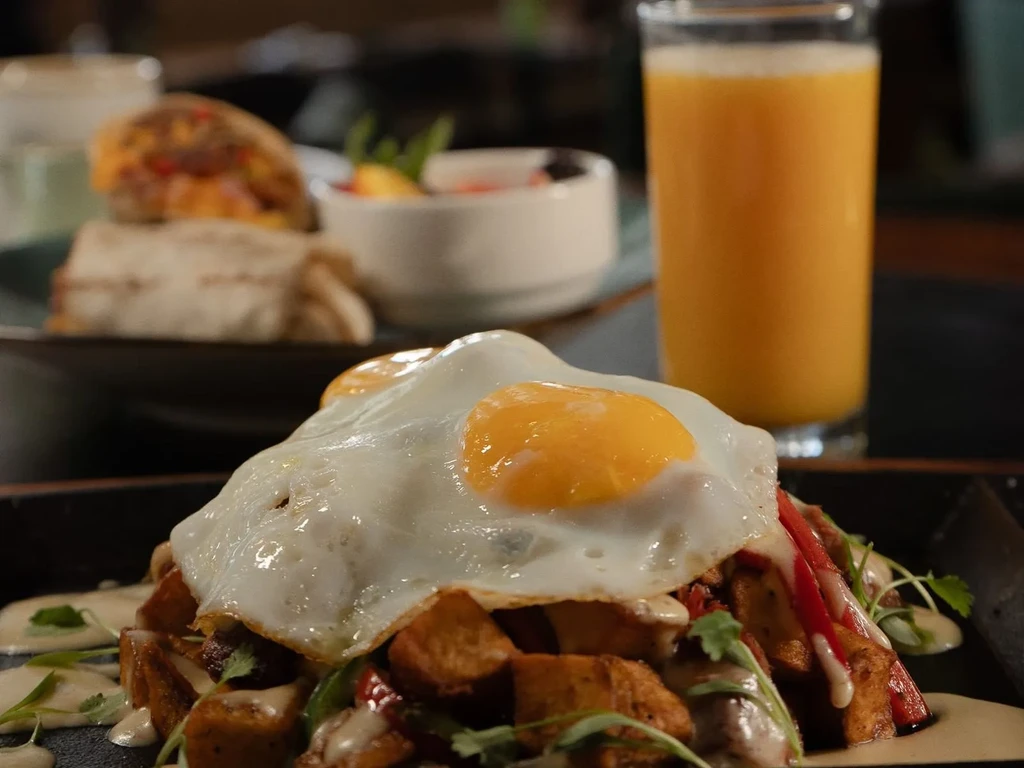 Breakfast meal: fried eggs, roasted potatoes, peppers, creamy sauce.