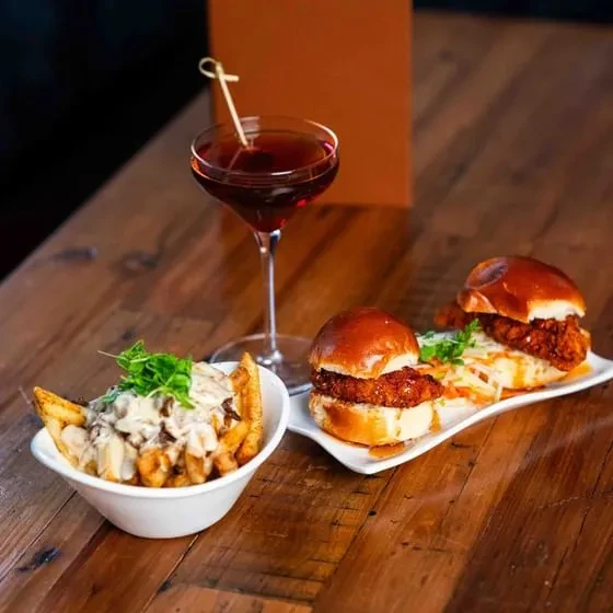Mini burgers, sauced fries, and a red cocktail on a rustic wooden table.