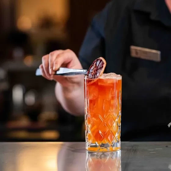 A bartender garnishes an orange cocktail with a dried citrus slice.