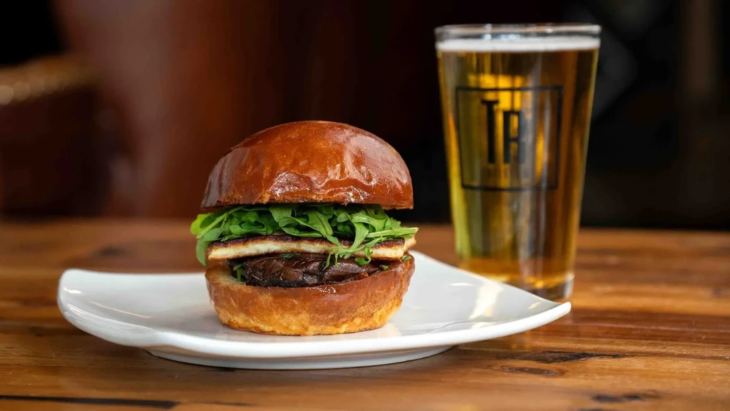 Close-up: Gourmet veggie burger, cheese, arugula, and glass of beer.