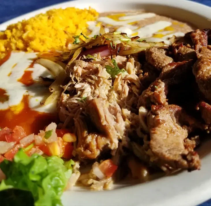 A close-up of a Mexican combo platter with rice, beans, and meats.