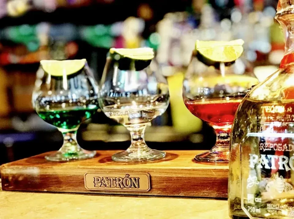 Three cocktails with lime on a Patrón branded tray with a tequila bottle.