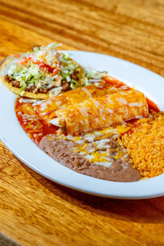 Plate of enchiladas with red sauce, rice, refried beans, and tostada.
