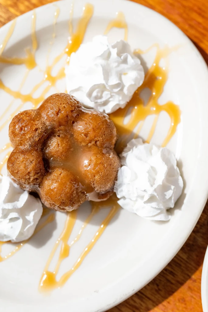 Golden-brown flower pastry with caramel glaze, whipped cream on a white plate.