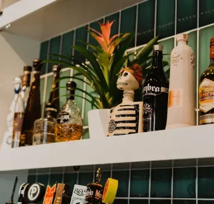 Well-stocked bar shelf with spirits, plant, skeleton figure, and beer taps.