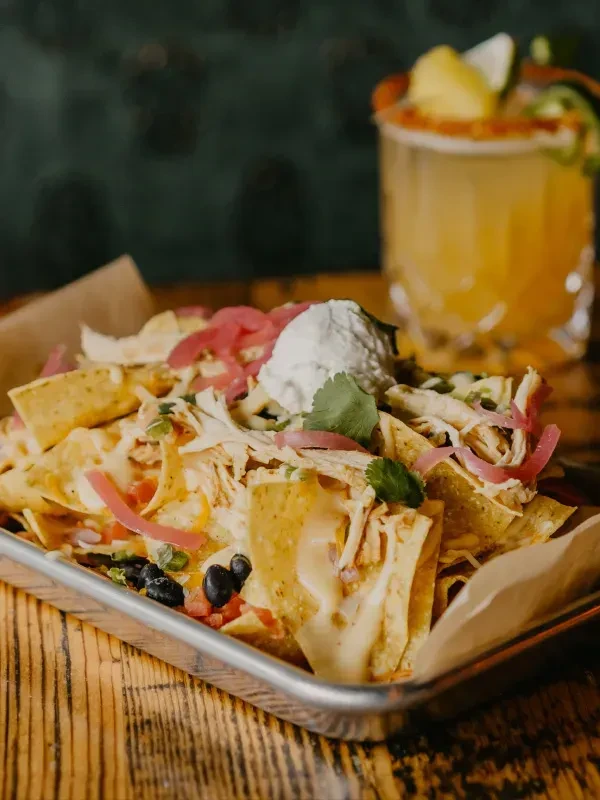 Platter of nachos with chicken, cheese, beans, and a cocktail.