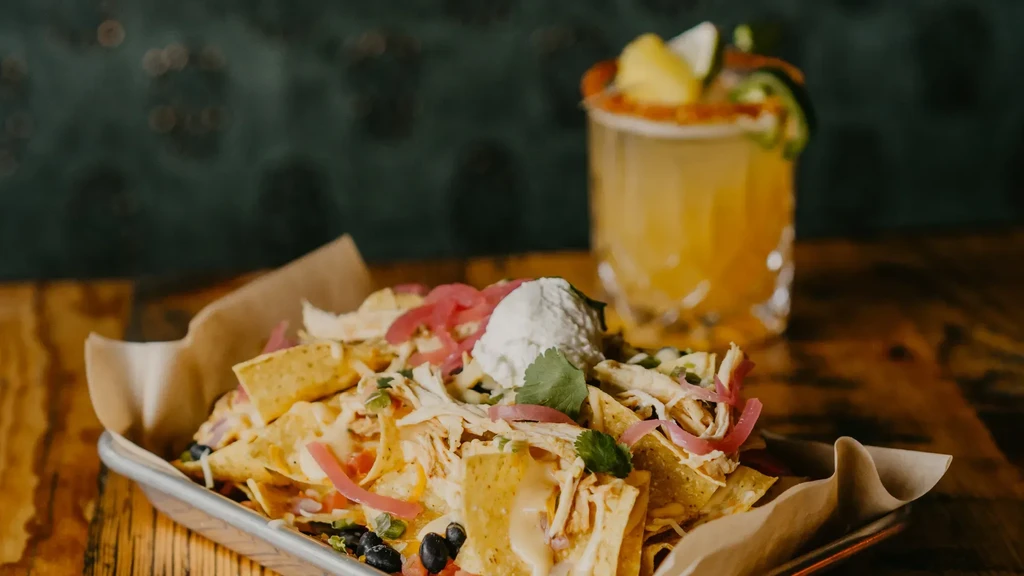 Loaded chicken nachos with melted cheese and black beans, blurred cocktail.