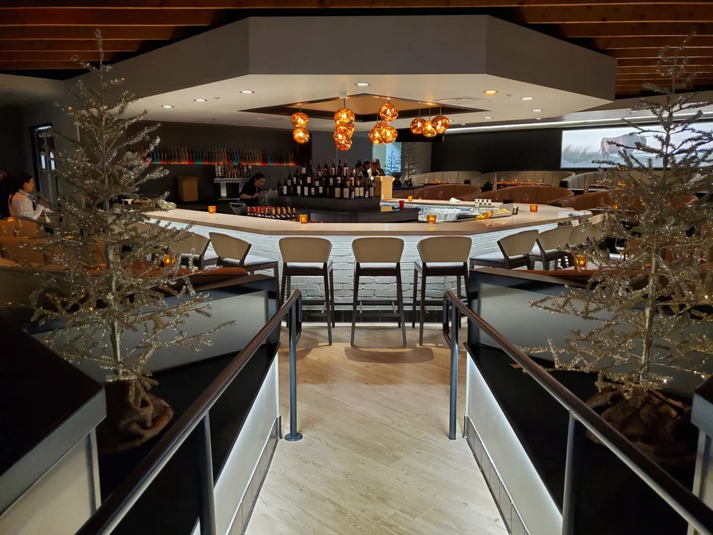 Upscale modern semi-circular bar with bartender, booths, festive trees.