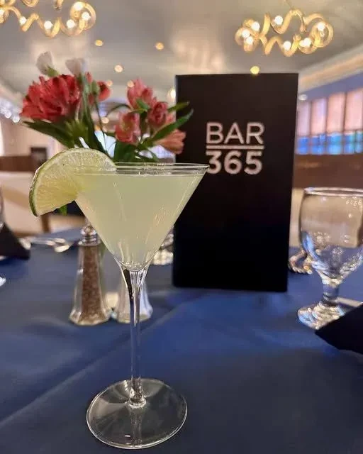 Light green cocktail with lime and "BAR 365" sign on table.