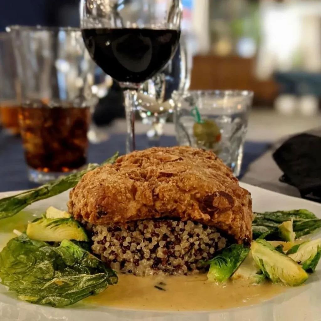 Golden-brown entree with quinoa, vegetables, and sauce on a white plate.