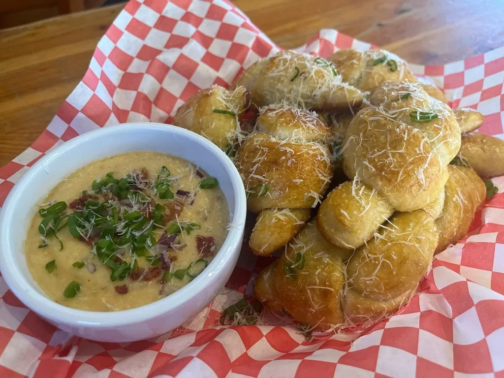 Basket of golden-brown bread knots, Parmesan, herbs, and creamy dip.