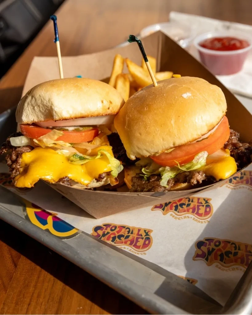 Two smash burgers, fries, and ketchup on branded paper.