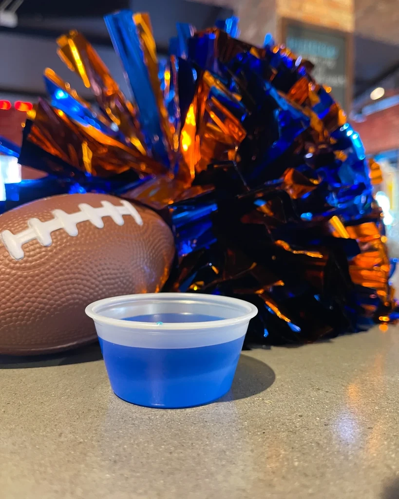 Brown football, blue/orange pom-pom, blue drink cup on a gray counter.