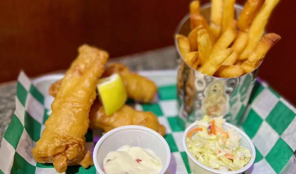 Battered fish, fries, lemon, tartar sauce, and coleslaw on a tray.