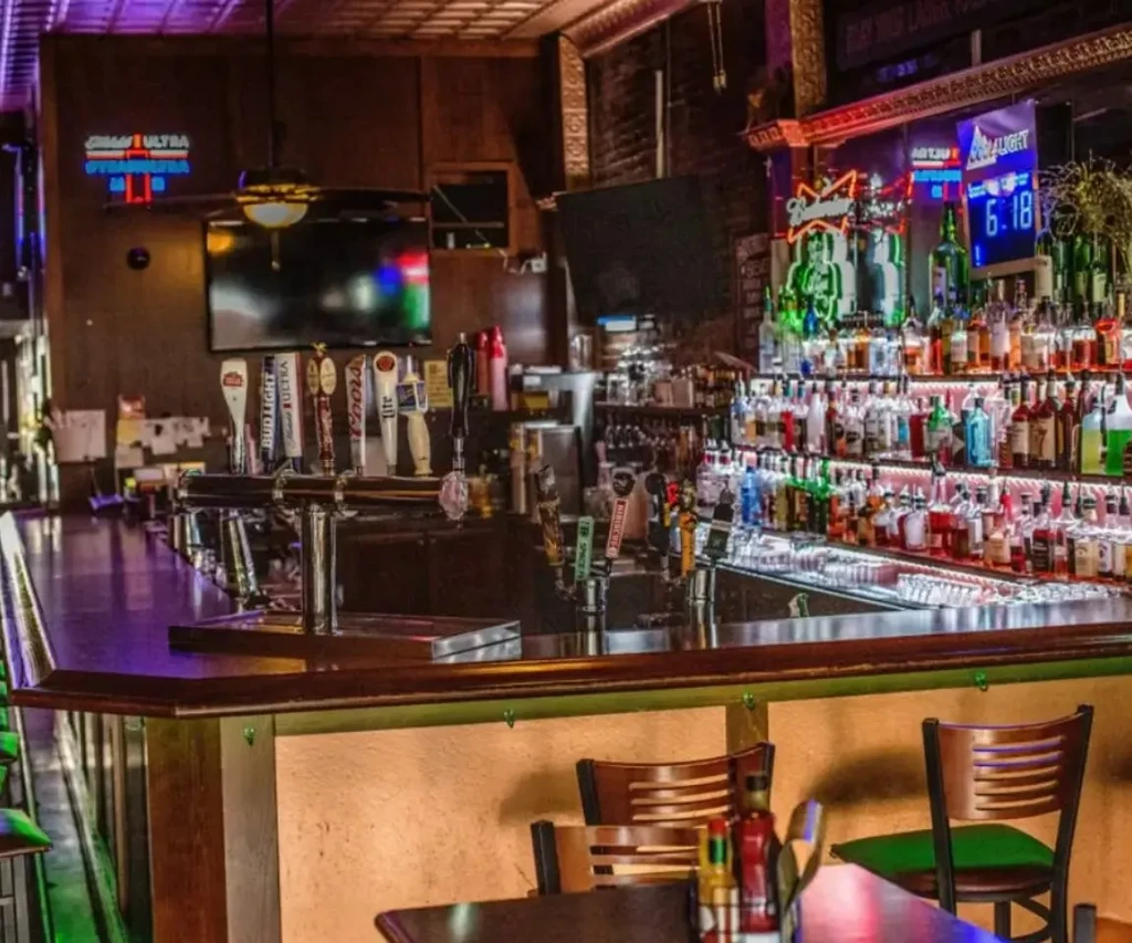 Atmospheric bar with dark counter, beer taps, and glowing liquor bottles.
