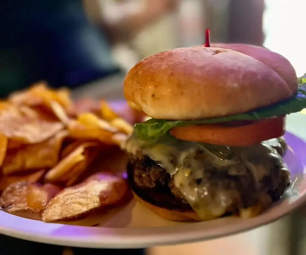 Close-up of a gourmet cheeseburger, lettuce, tomato, and potato chips.