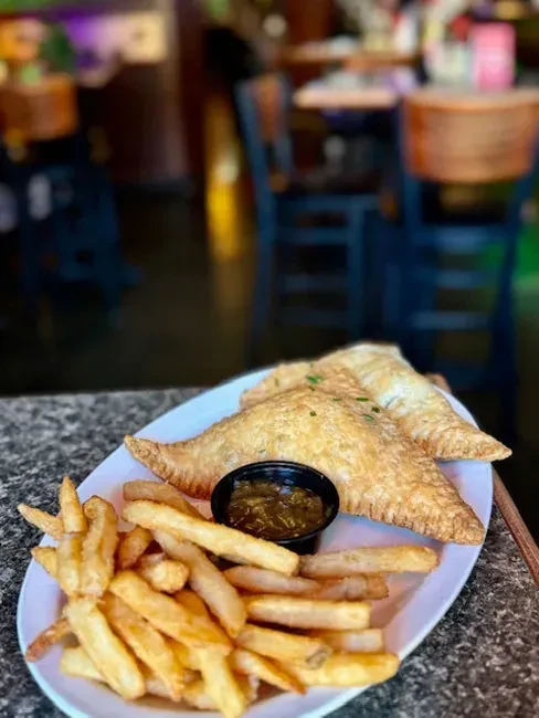 Golden pastries, crispy french fries, and green relish on a plate.