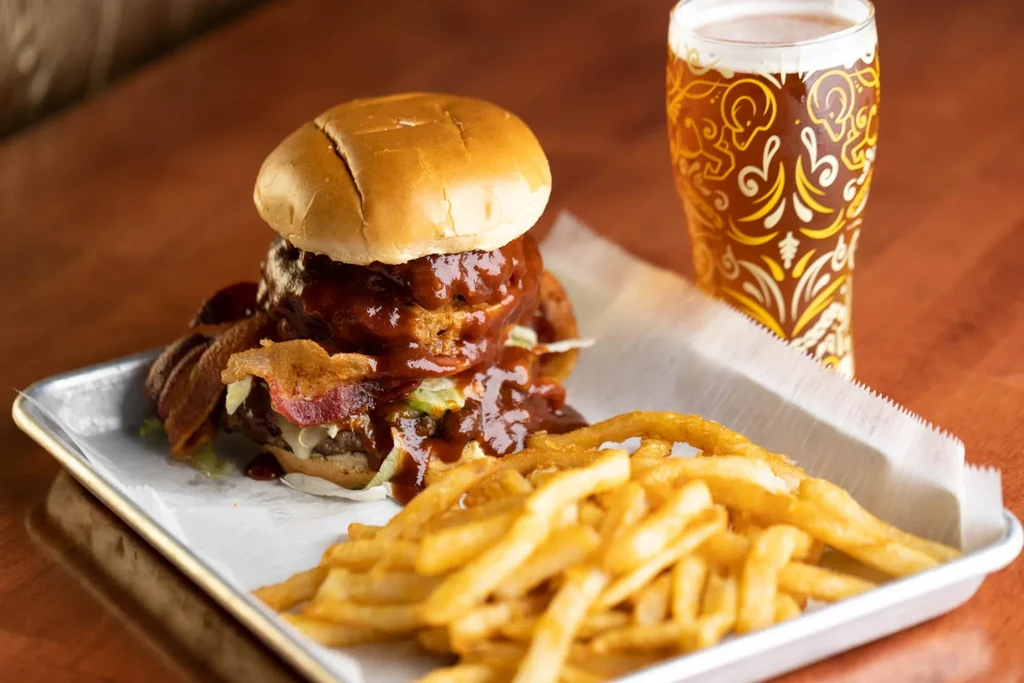 A large BBQ burger, crinkle fries, and beer on a tray.